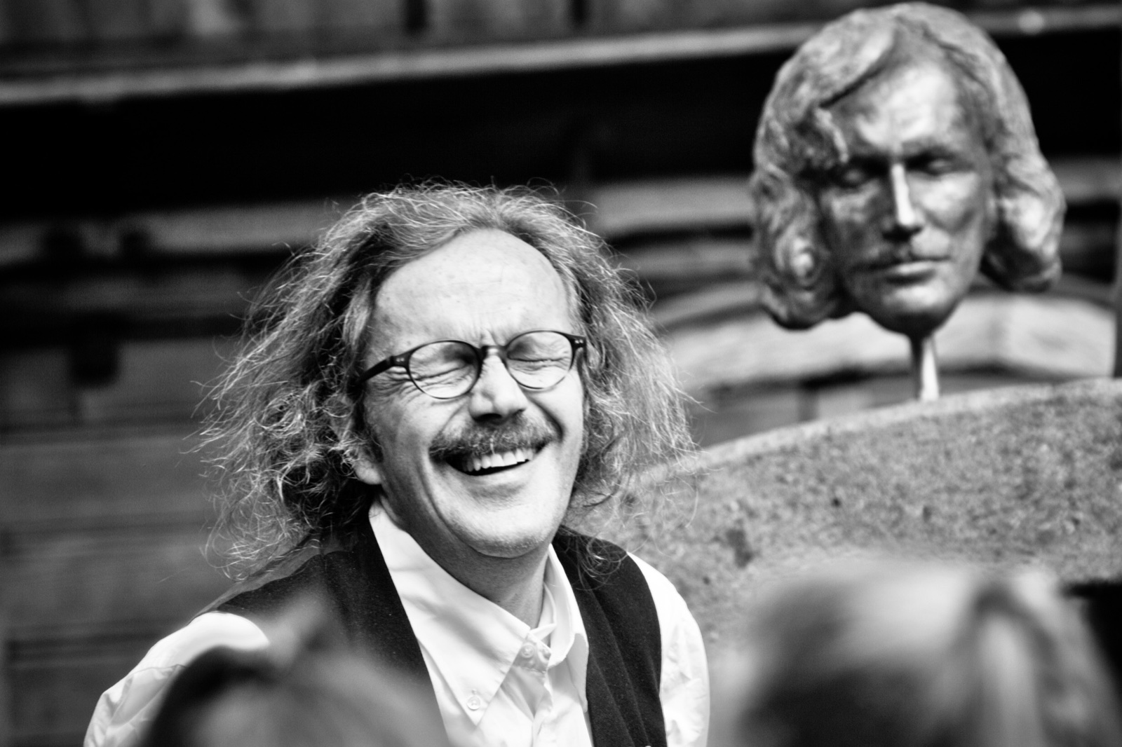 Heinz Bömler lachend neben einer historischen Büste, Schwarzweißporträt